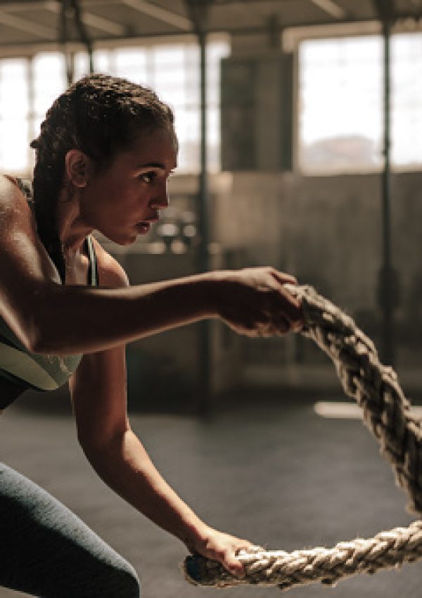 Powerful muscular woman exercising with battle ropes at the gym with personal trainer. Battle rope workout at gym with instructor.